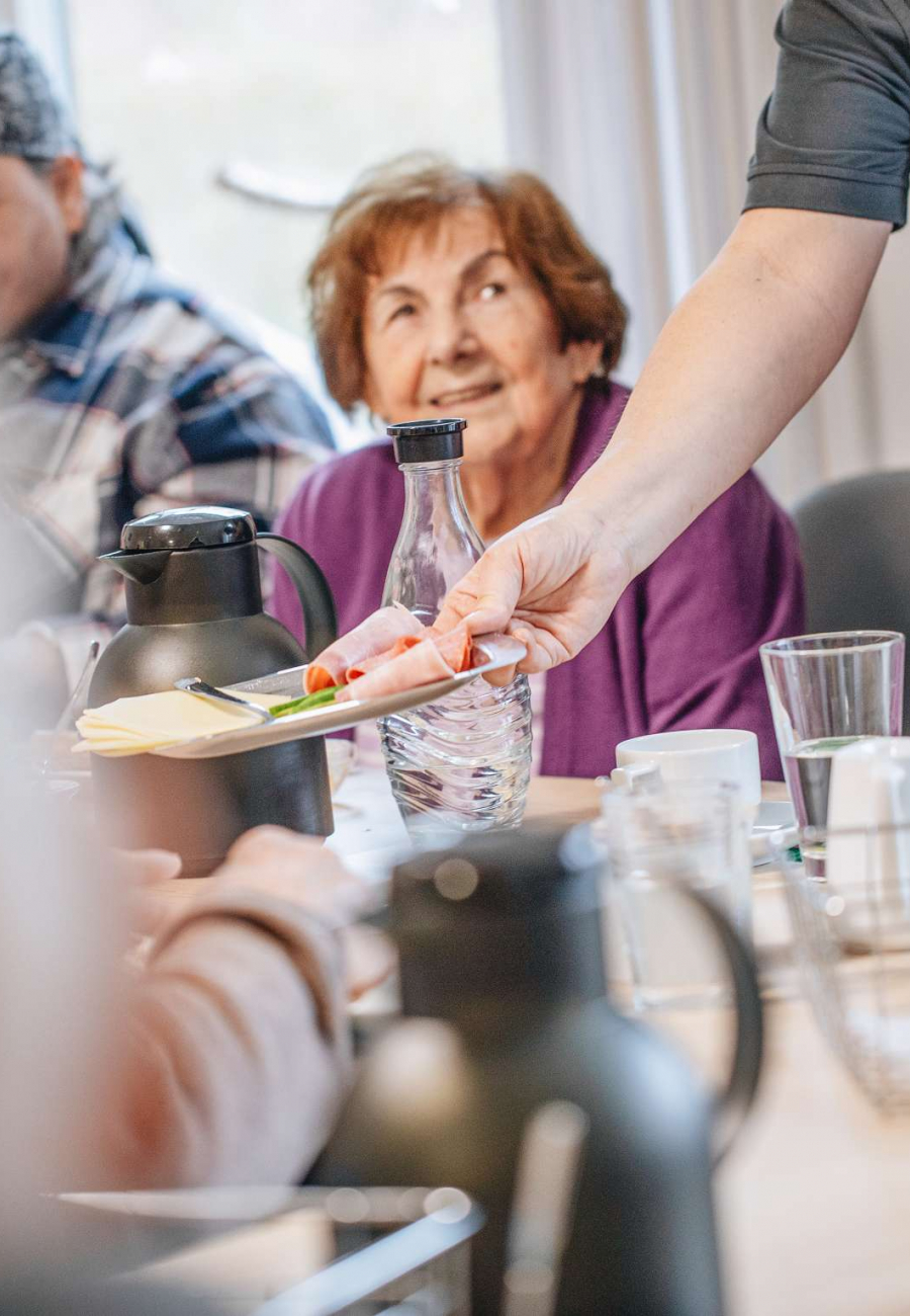 Alte Dame am Tisch wird Essen gereicht